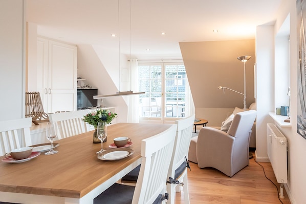 Een moderne keuken met witte kastjes, een houten eettafel en een uitzicht buiten door grote ramen.
