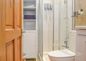Kylpyhuoneessa on lasiseinäinen suihkukaappi, wc ja seinään upotettu hylly, jossa on hygieniatuotteita.