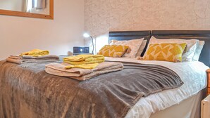 A neatly made bed with a grey and white duvet, multiple folded towels, and patterned pillows. - 1 bedroom accommodation in Dolgellau (Dolgellau)