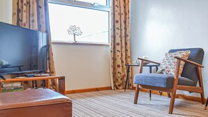 A room with a television, a chair, a small table, and a window with curtains. - 1 bedroom accommodation in Dolgellau (Dolgellau)
