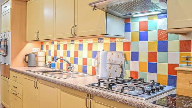 A kitchen with beige cabinets, a gas stove, a sink, and a colorful tile backsplash. - 1 bedroom accommodation in Dolgellau (Dolgellau)