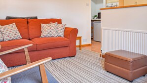 A living room with a sofa, a small table, a bench, and a kitchen area with cabinets and appliances. - 1 bedroom accommodation in Dolgellau (Dolgellau)