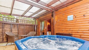 A wooden cabin with a hot tub, wicker chairs, and a wooden deck. - Cobbett Traditional Premier (Tilford, Farnham)