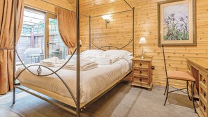 A four-poster bed in a wooden room with a painting on the wall and a small table with drawers. - Cobbett Traditional Premier (Tilford, Farnham)