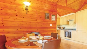 A wooden cabin interior with a dining table set for breakfast, a kitchen area, and a ceiling with exposed beams. - Cobbett Traditional Premier (Tilford, Farnham)