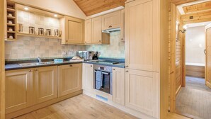 A kitchen with wooden cabinets, a microwave, and a built-in oven. - Cobbett Traditional Premier (Tilford, Farnham)