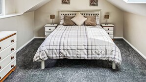 A bedroom with a sloped ceiling, a bed with a plaid bedspread, two bedside tables with lamps, a dresser, and two wall-mounted pictures. - 3 bedroom accommodation in Buxton (Buxton)