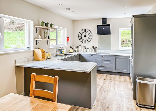 A modern kitchen with a central island, grey cabinets, a built-in oven, and a large window.