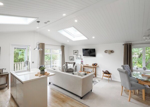 A spacious living area with a central island, a dining table, and a TV mounted on the wall. - Kielder Forest Lodge (Kielder)