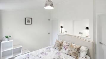 A bedroom with a bed, a bedside table, a hanging light fixture, and a framed picture on the wall.