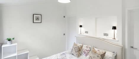 Un dormitorio con cama, mesita de noche, lámpara colgante y un cuadro en la pared.