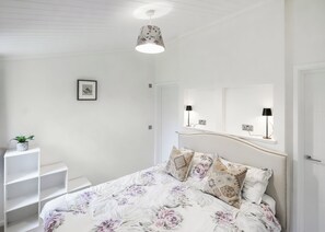 Un dormitorio con cama, mesita de noche, lámpara colgante y un cuadro en la pared.