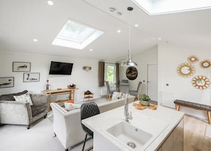 A modern kitchen with a central island, a dining area with a sofa and table, and a living room with a TV and artwork. - Kielder Forest Lodge (Kielder)