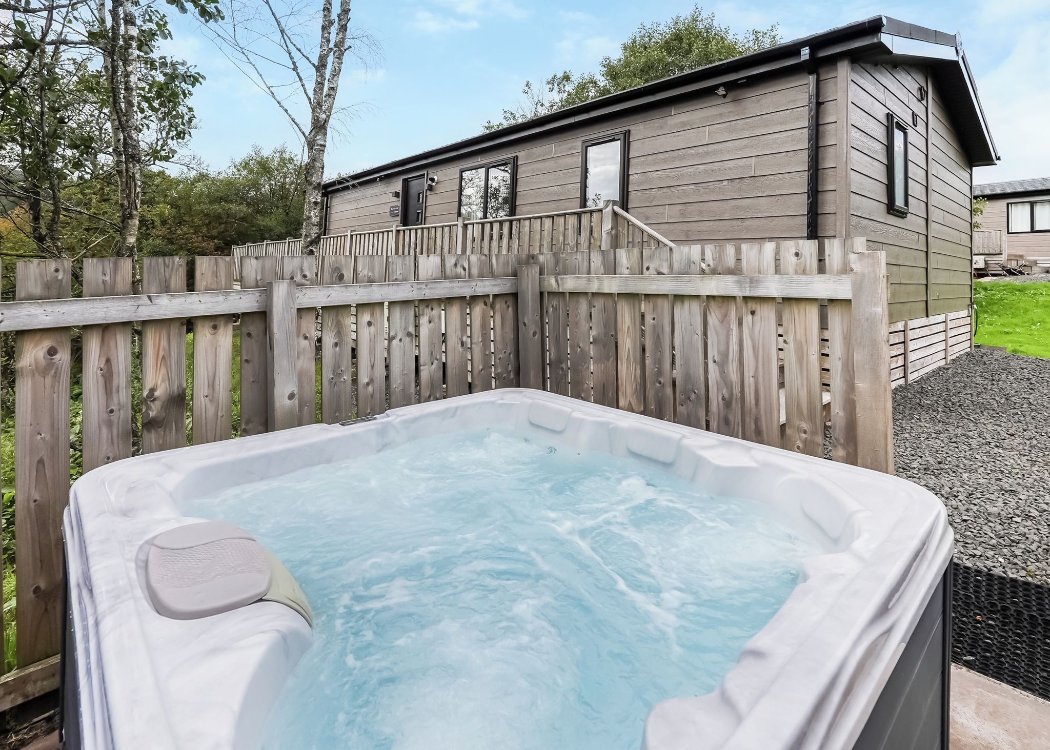 A hot tub in a backyard with a wooden fence and a house in the background.