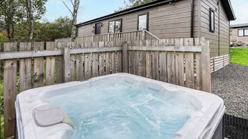 A hot tub in a backyard with a wooden fence and a house in the background.