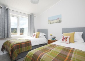 A bedroom with two beds, a window with curtains, a painting on the wall, and a nightstand with a lamp and a toy car.