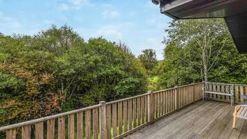 A wooden deck with a railing, surrounded by dense greenery and trees.