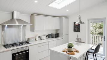 A modern kitchen with white cabinetry, a stainless steel range hood, a gas stove, a microwave, and a small island with a plant.