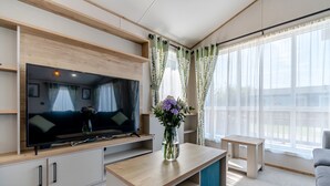 A modern living room with a flat-screen TV, a coffee table, a sofa, and a large window with sheer curtains. - 4 bedroom accommodation in Skegness (Skegness)