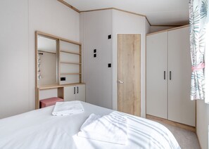 A bedroom with a bed, a wooden wardrobe, a mirror, and a small bench.