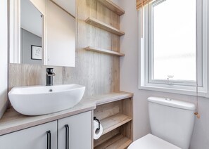 A bathroom with a white sink, wooden shelves, a toilet, and a window with a view. - 4 bedroom accommodation in Skegness (Skegness)