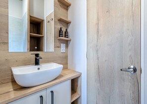 A bathroom with a white sink, wooden vanity, a mirror, and a wooden door.