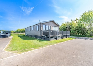 A single-story mobile home with a fenced patio area, a small attached structure, and a paved driveway. - 4 bedroom accommodation in Skegness (Skegness)