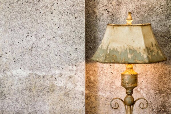Une lampe avec un abat-jour usé, placée sur un mur à la texture particulière.