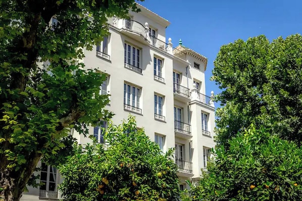 Een meerlaags gebouw met balkons, omringd door weelderige groene bomen en oranje herfstbladeren.