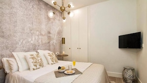 A bedroom with a bed, bedside table, lamp, and a television on the wall. - Terrace Suite City Center (Granada)