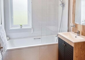 Un baño moderno con bañera, ducha, lavamanos y una ventana con una planta.