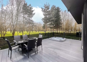 Une terrasse dotée de mobilier d’extérieur et d’un jacuzzi, offrant une vue sur un espace verdoyant avec des arbres.
