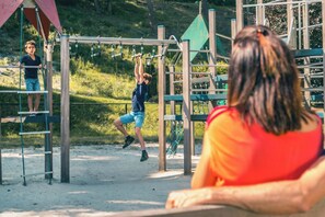 Explore the playground with a climbing frame and swing set amidst lush green surroundings.