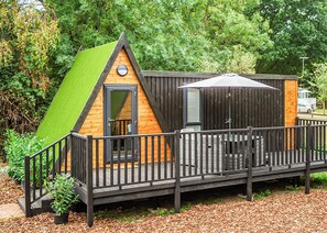 A small wooden cabin with a green roof, a deck, and a fenced patio area. - 1 bedroom accommodation in Sewardstone (Sewardstone)