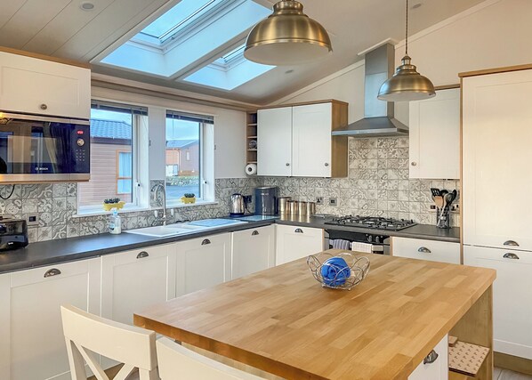 A modern kitchen with a skylight, a Bosch microwave, a coffee maker, and a wooden dining table.