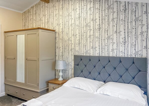 A bedroom with a bed, a wardrobe, a nightstand, and a lamp.