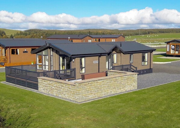 A row of modern, two-story cabins with large windows and a stone foundation, set in a grassy area with a clear sky.