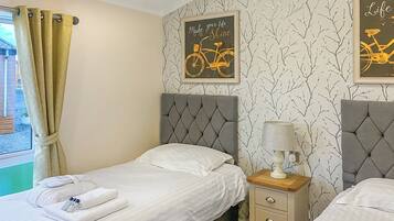 A bedroom with two beds, a window with curtains, a wall with a bicycle-themed poster, and a bedside lamp.
