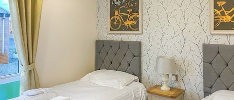 Ein Schlafzimmer mit zwei Betten, einem Fenster mit Vorhängen, einer Wand mit einem Fahrrad-Poster und einer Nachttischlampe.