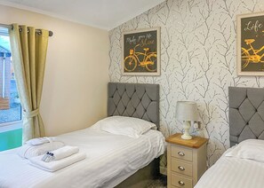 Ein Schlafzimmer mit zwei Betten, einem Fenster mit Vorhängen, einer Wand mit einem Fahrrad-Poster und einer Nachttischlampe.