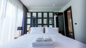 Et hotelværelse med en stor seng, et natbord, en lampe og udsigt til et badeværelse adskilt af glas.