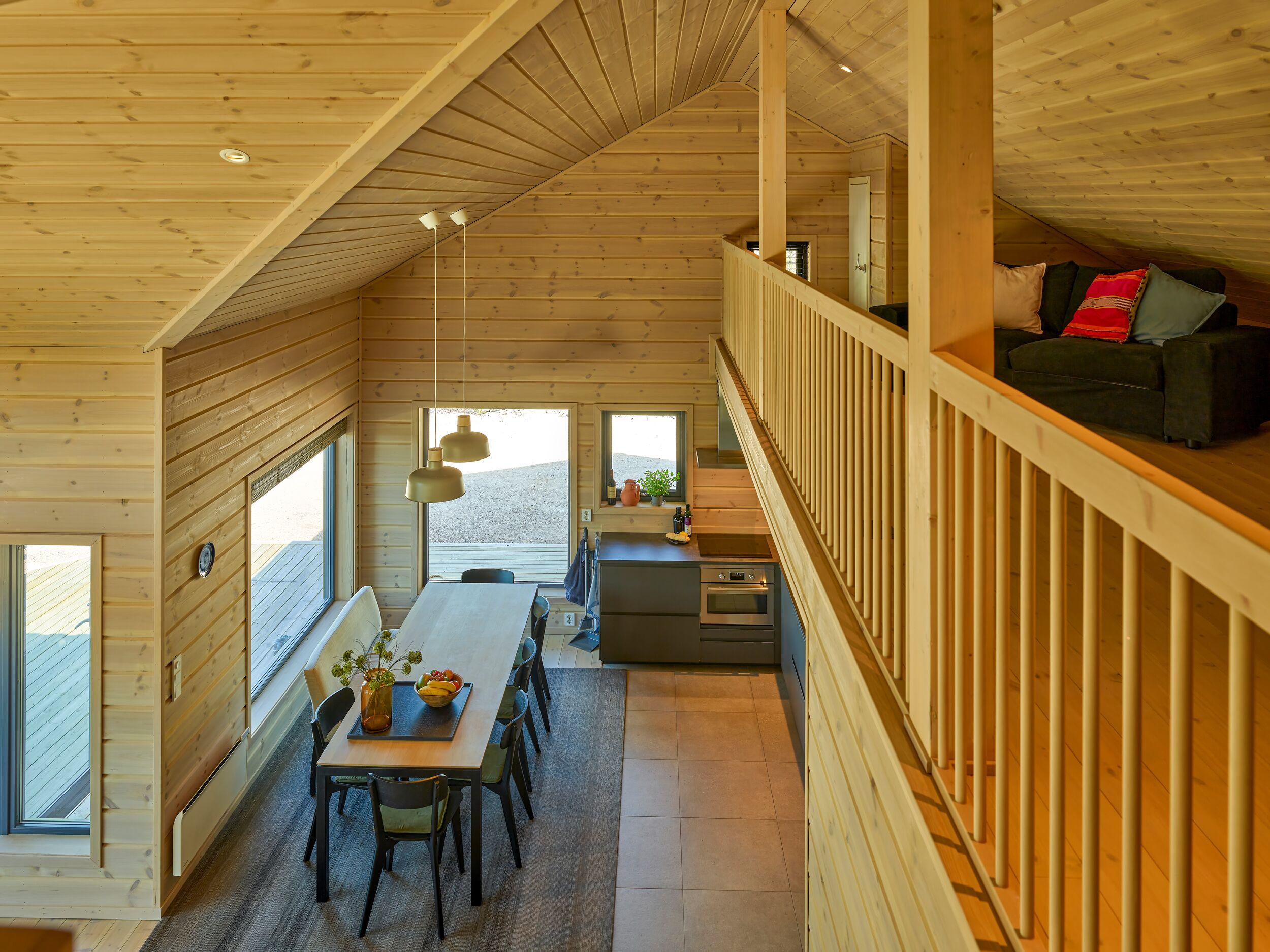 A cozy cabin with a dining area, kitchen, and a loft bedroom with a sofa.