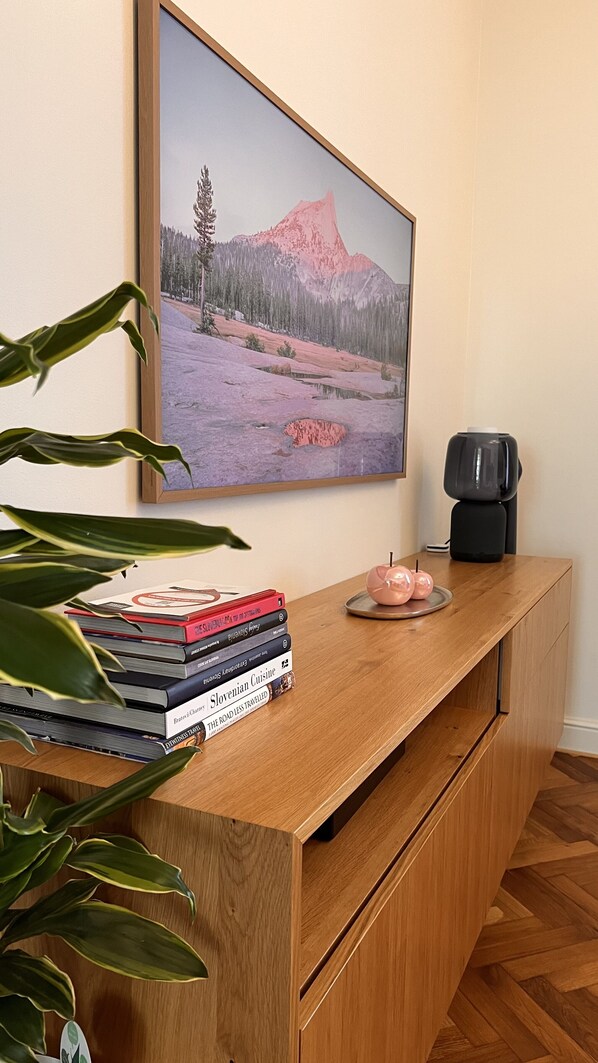 A wooden desk with a stack of books, a coffee maker, and a framed landscape painting.