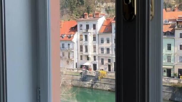 A window with a view of a town, including buildings and a hill with a tower. - Riverside Apartment Ljubljana with free parking (Ljubljana)