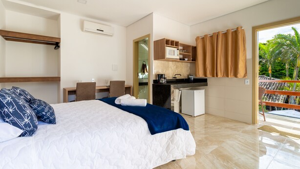 Una camera d'albergo moderna con un letto, una scrivania, angolo cottura e un balcone con vista sulle palme.