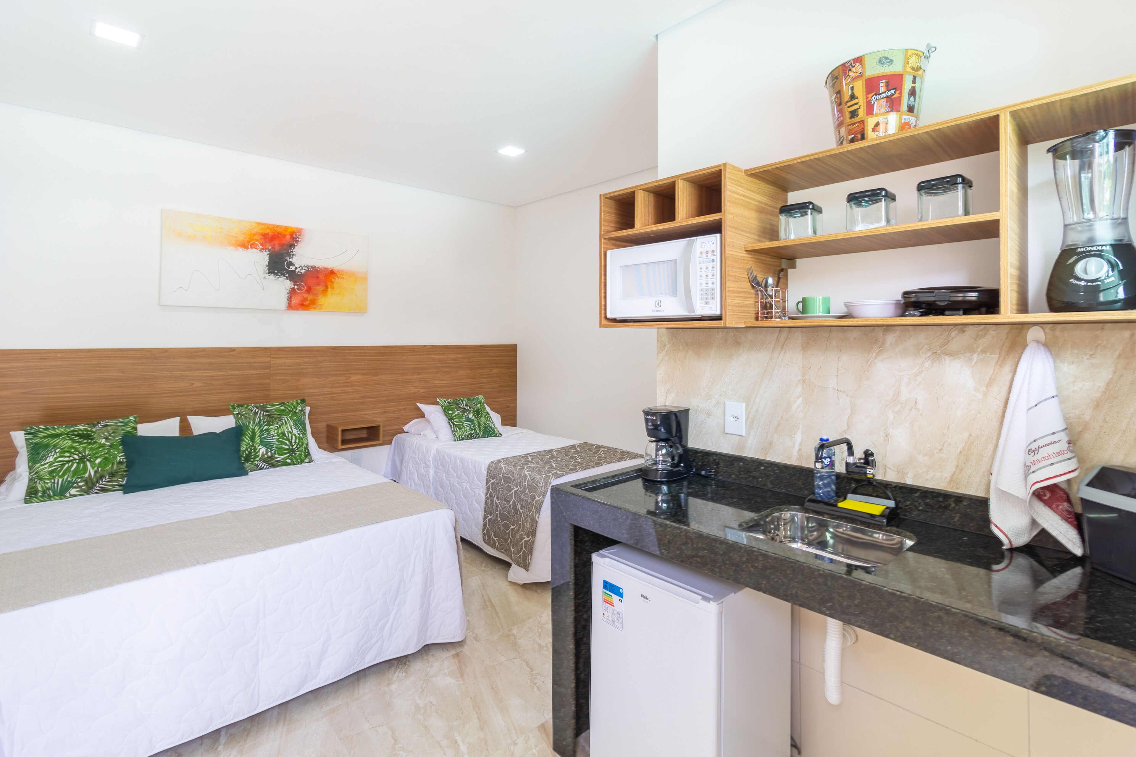 Habitación de hotel con dos camas, kitchenette, microondas, licuadora y refrigerador pequeño.