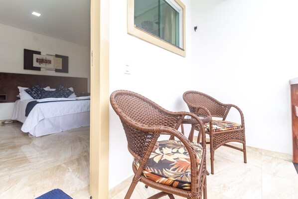 Ein Hotelzimmer mit einem Bett, zwei Korbstühlen mit Blumenkissen, einer Holzkommode und einem gerahmten Bild an der Wand.
