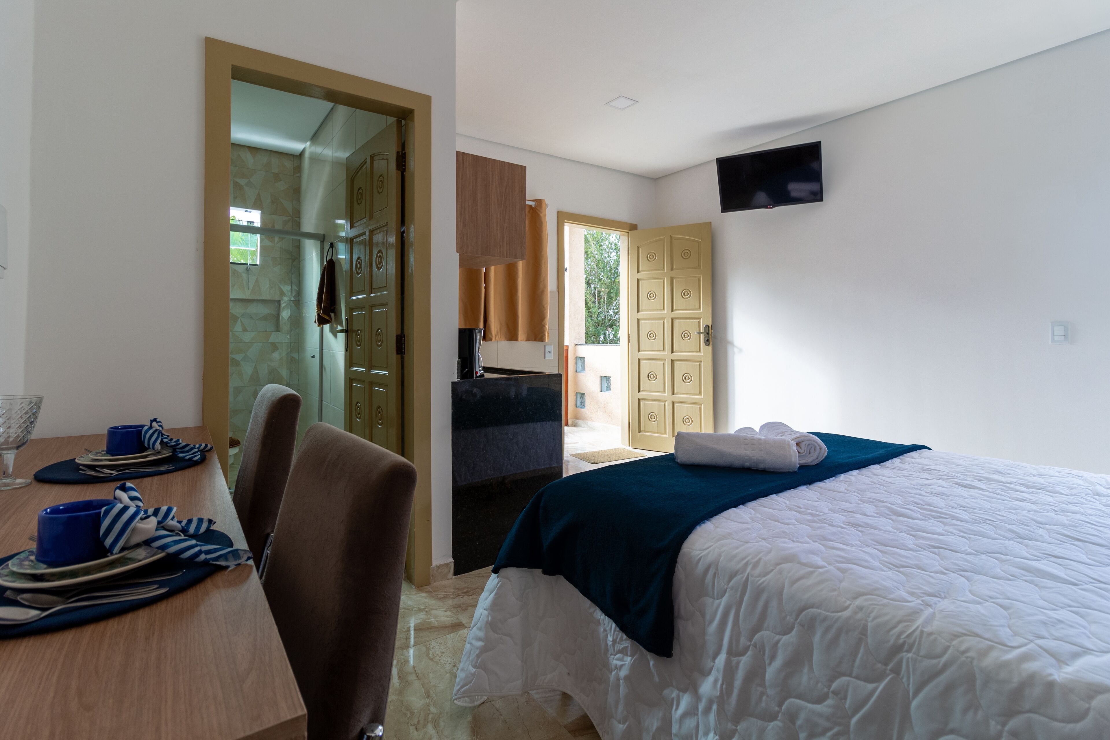 A hotel room with a bed, a desk with a chair, a television mounted on the wall, and a bathroom visible through an open door.