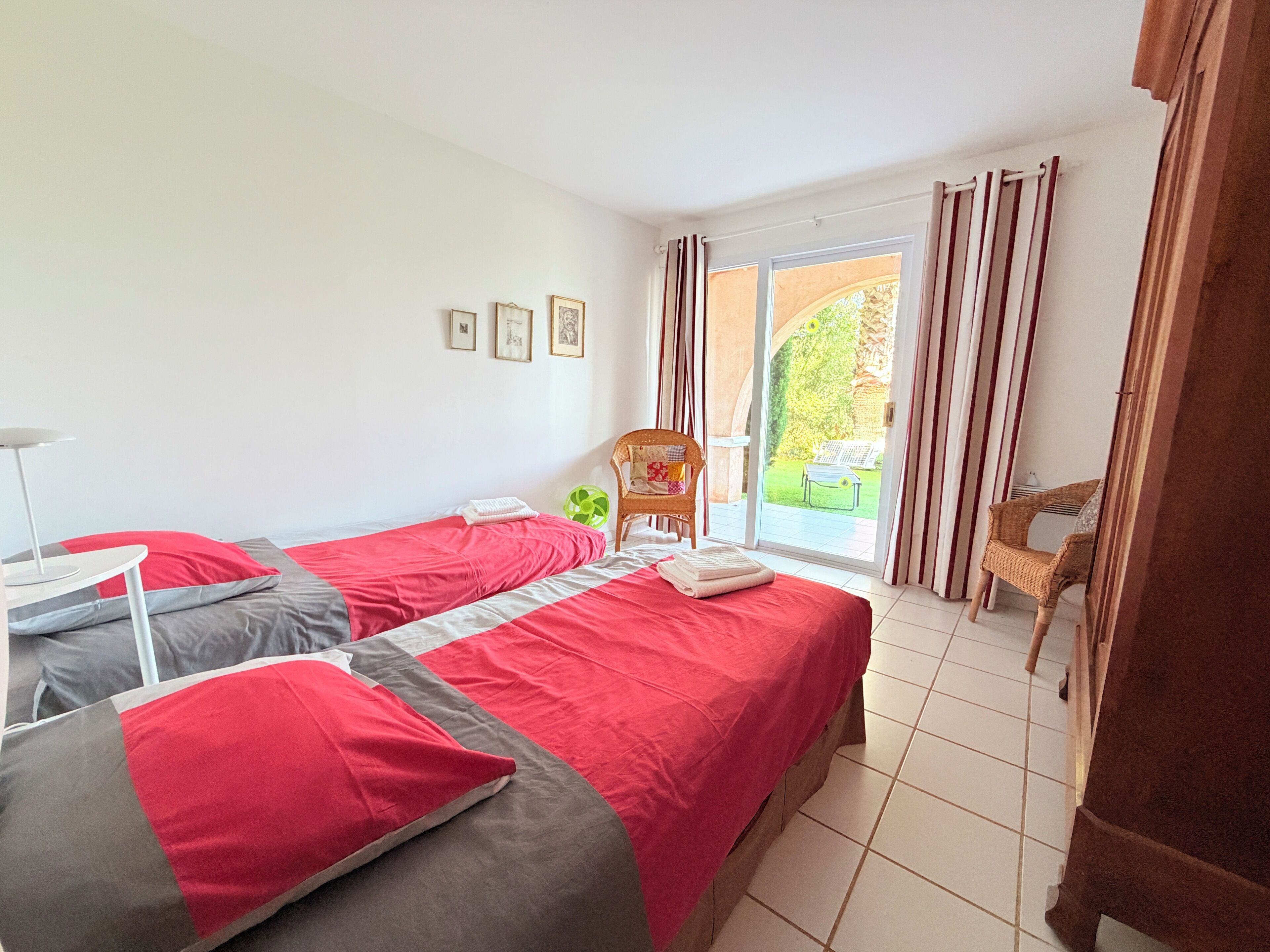 Een hotelkamer met twee bedden, een stoel, een tafel en uitzicht op de tuin door het raam.