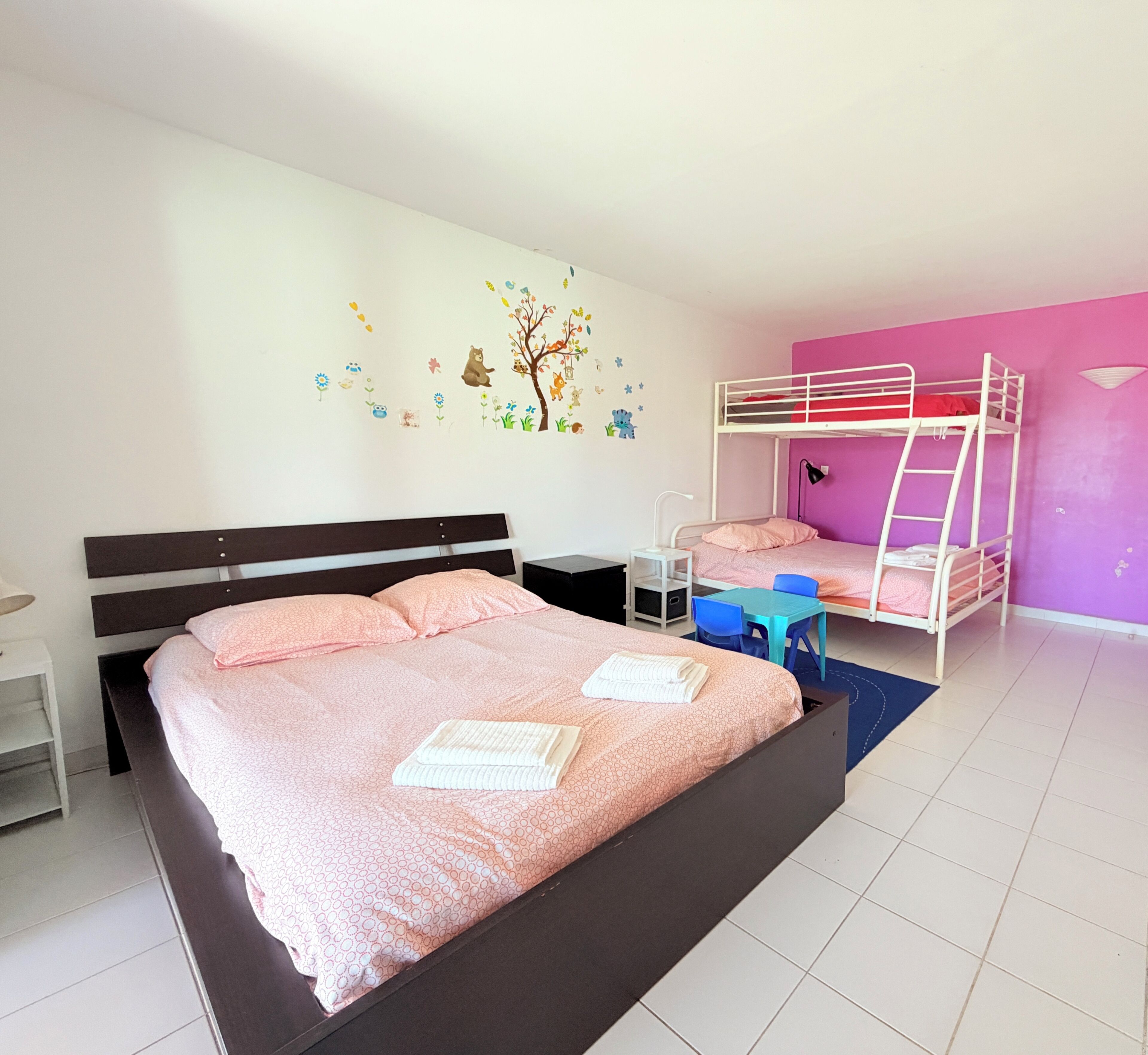 Une chambre avec un grand lit, un lit superposé plus petit, un bureau et une chaise.